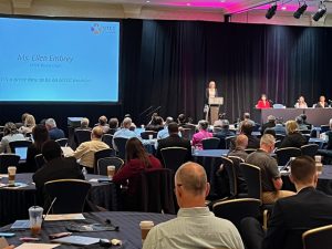 Photo of Ellen Embry on stage in front of a podium at the 7th Annual Meeting.